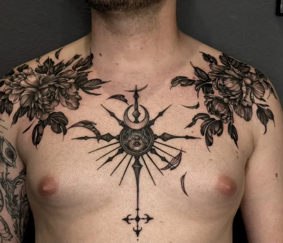Tatuaje en el pecho con un diseño floral y celestial simétrico en negro que abarca la parte superior del torso