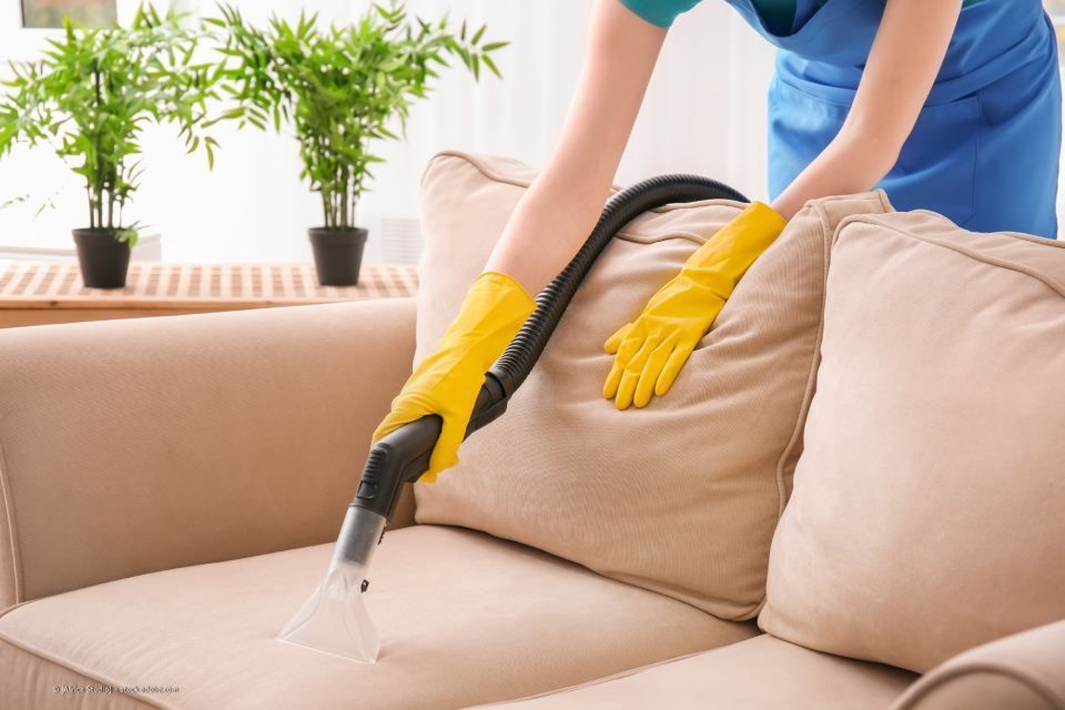 Reinigungskraft saugt ein Sofa