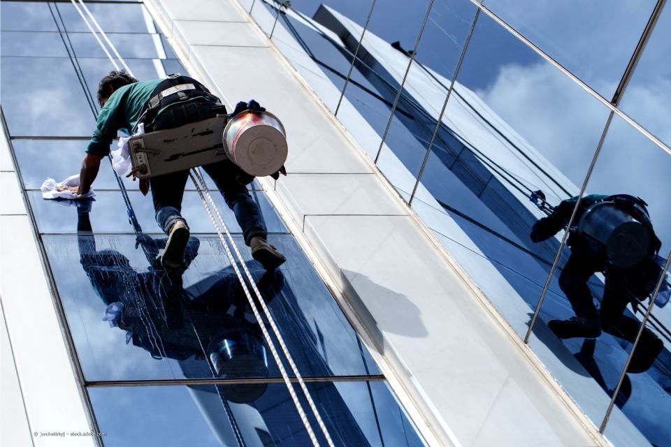 Person hängt am Seil an einer gläsernen Hausfassade