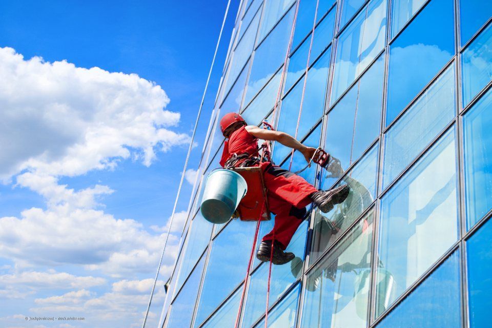 Fensterreinigungskraft hängt am Seil an einer gläsernen Hausfassade