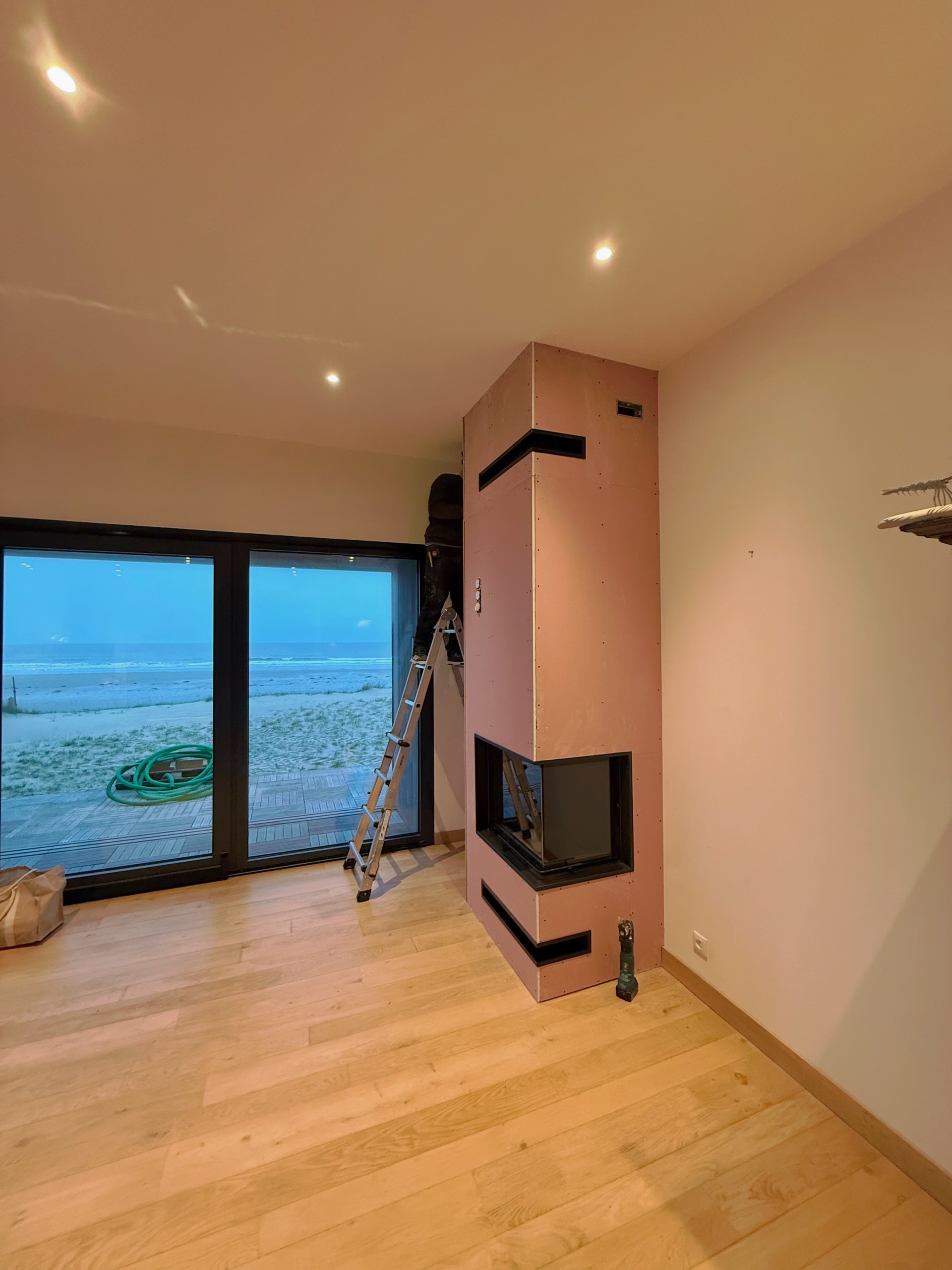 Cheminée moderne avec flammes dans une pièce blanche et grise en construction.