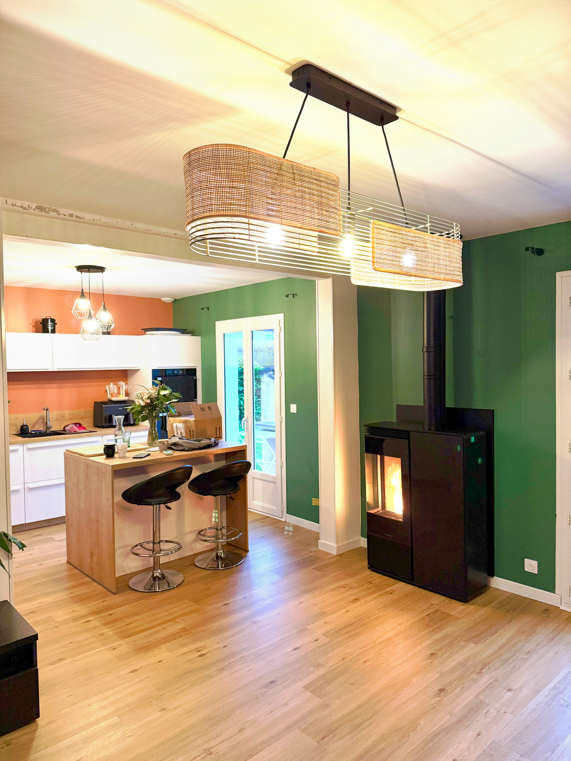 Cuisine spacieuse avec parquet, îlot central et tabourets de bar. Mur végétal avec cheminée.