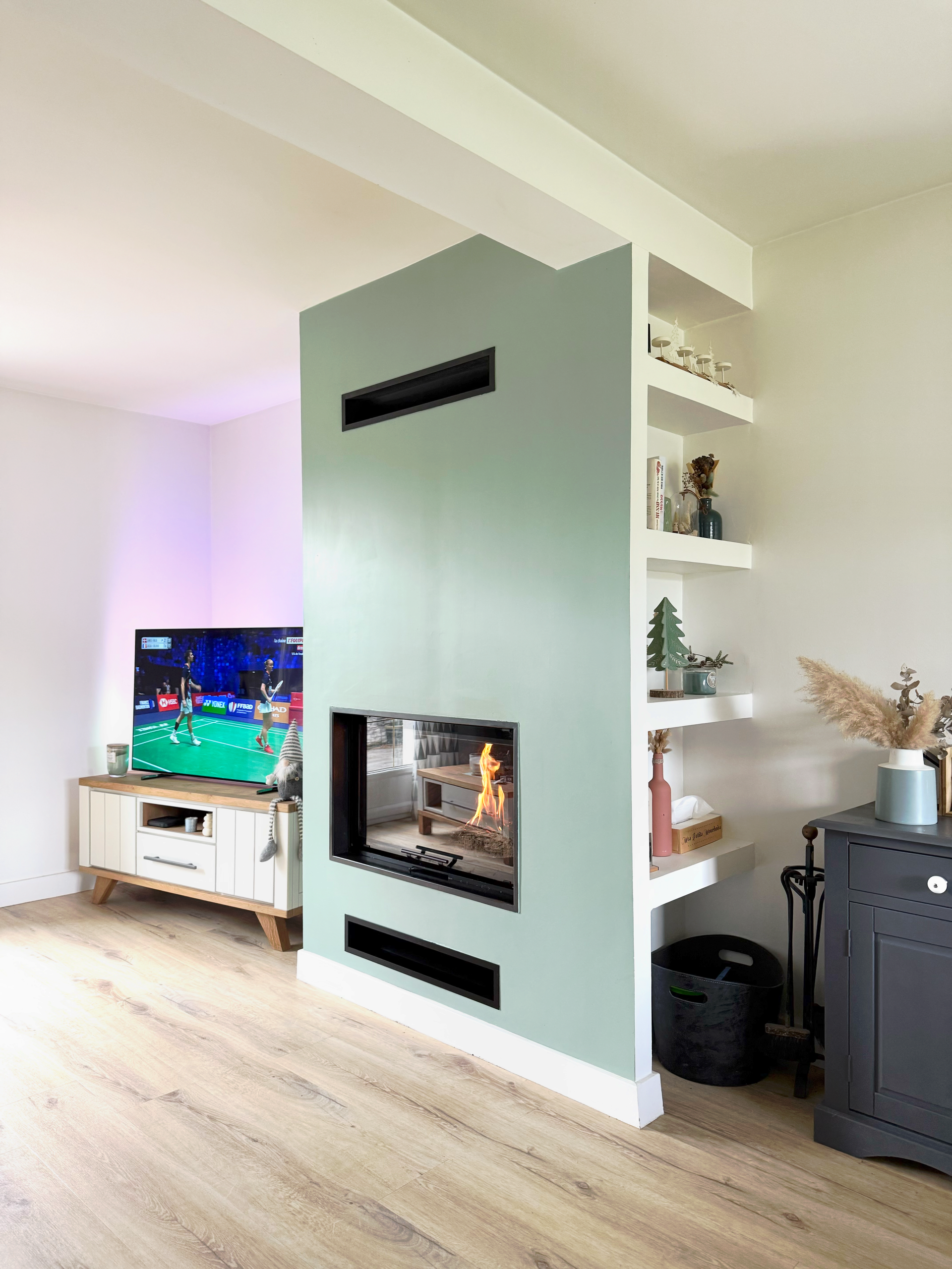 Salon avec cheminée, étagères et télévision sur un mur bleu turquoise.