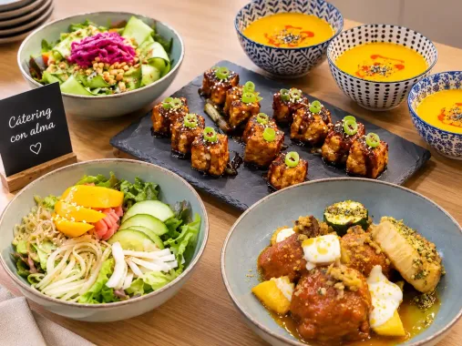Platos variados con ensaladas, brochetas a la parrilla y sopa de naranja sobre una mesa de comedor.