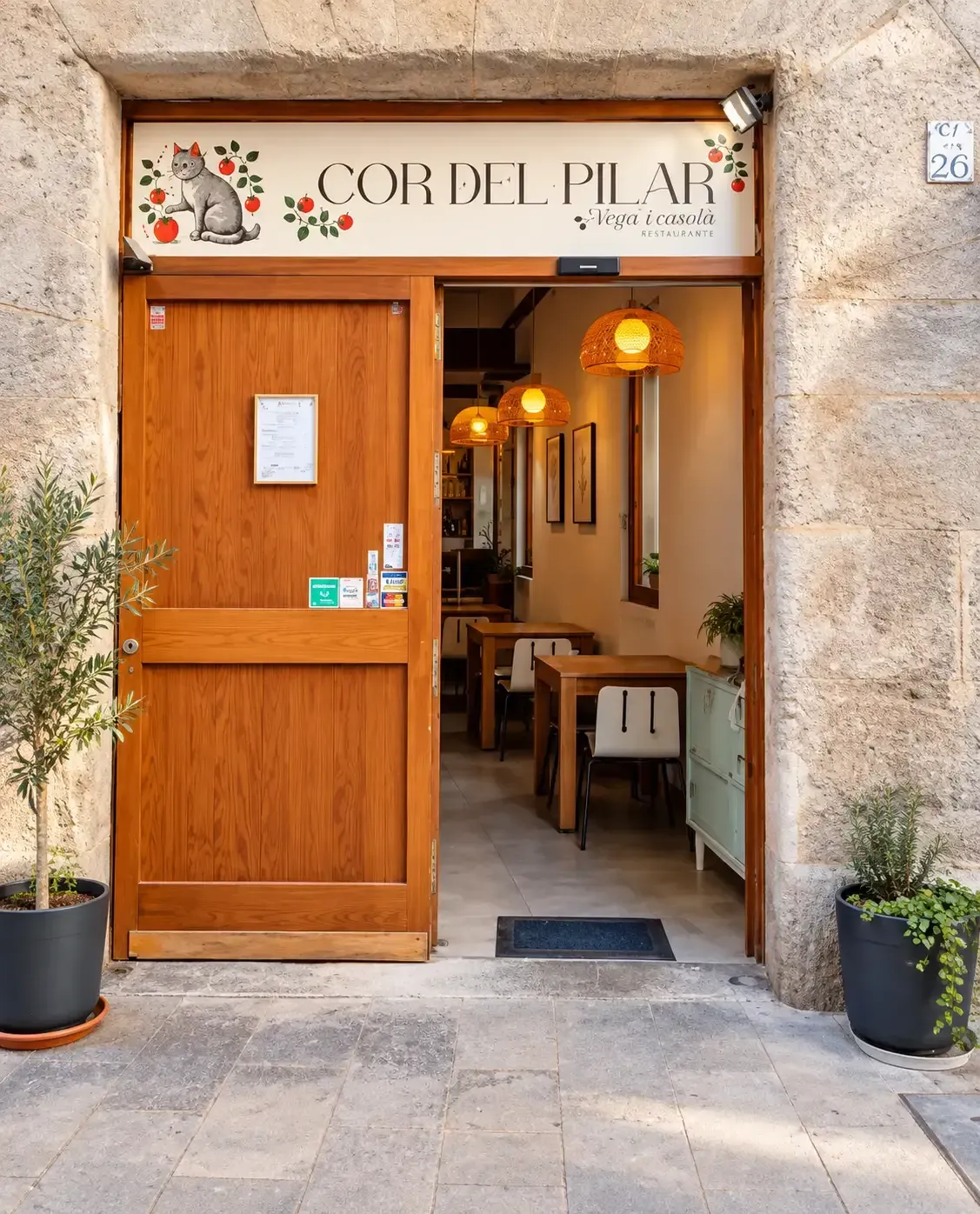 Una puerta de madera abierta da acceso a un acogedor restaurante con luces cálidas y plantas en macetas.