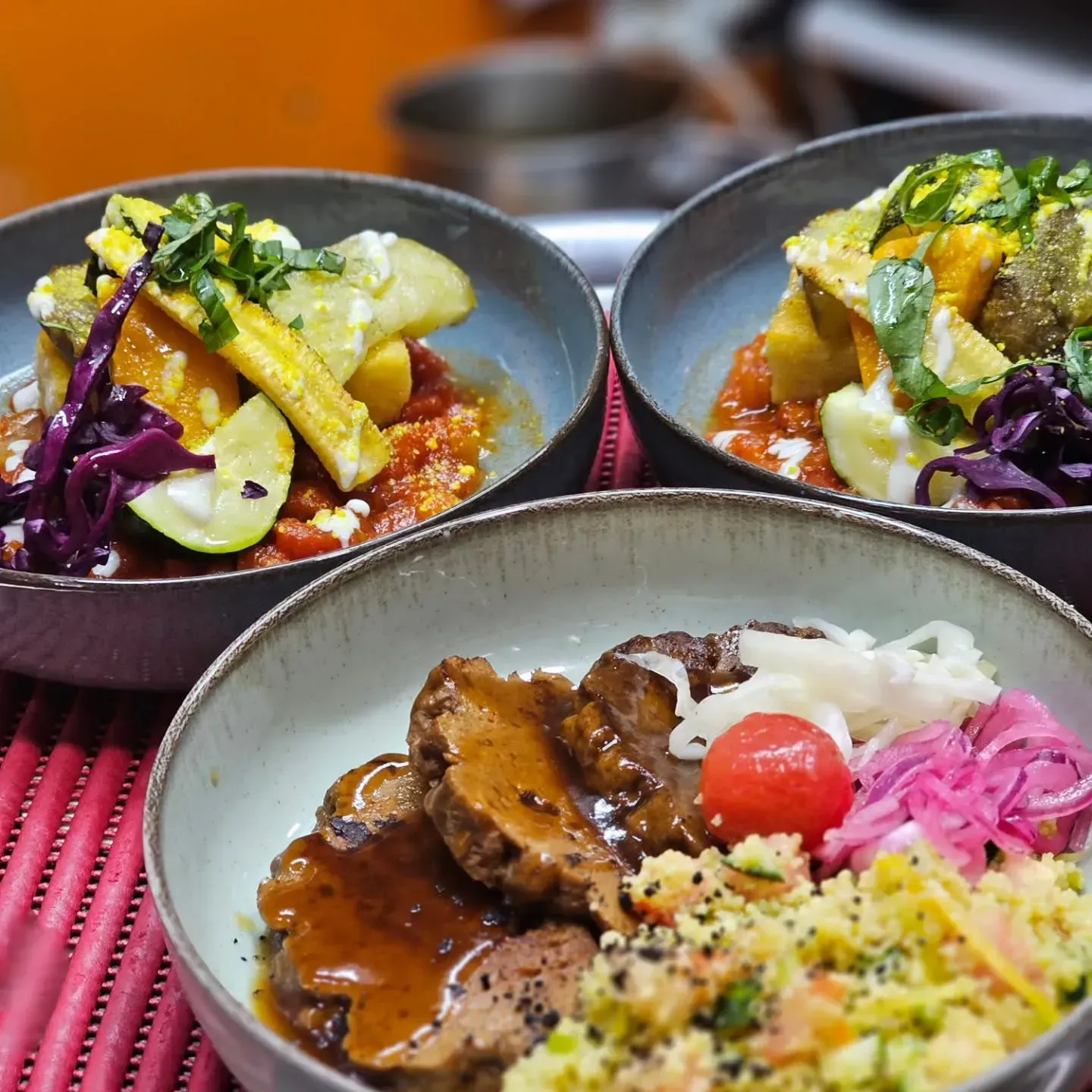 Tres platos coloridos servidos en la mesa, que incluyen curry, arroz y verduras en cuencos poco profundos.