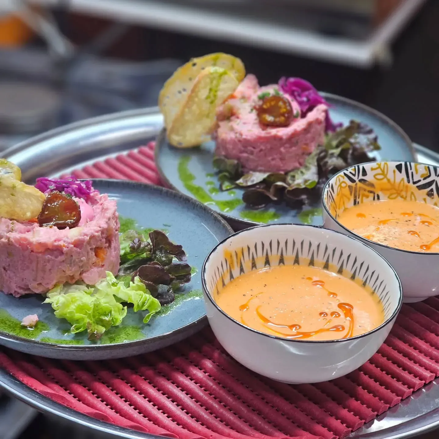 Dos ensaladas rosadas emplatadas con galletas saladas y salsa para mojar en una bandeja roja.