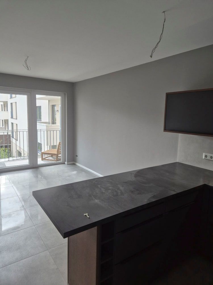 Leeres, modernes Wohnzimmer mit grauen Wänden, Fliesenboden, Balkontüren und einem an der Wand montierten Fernseher