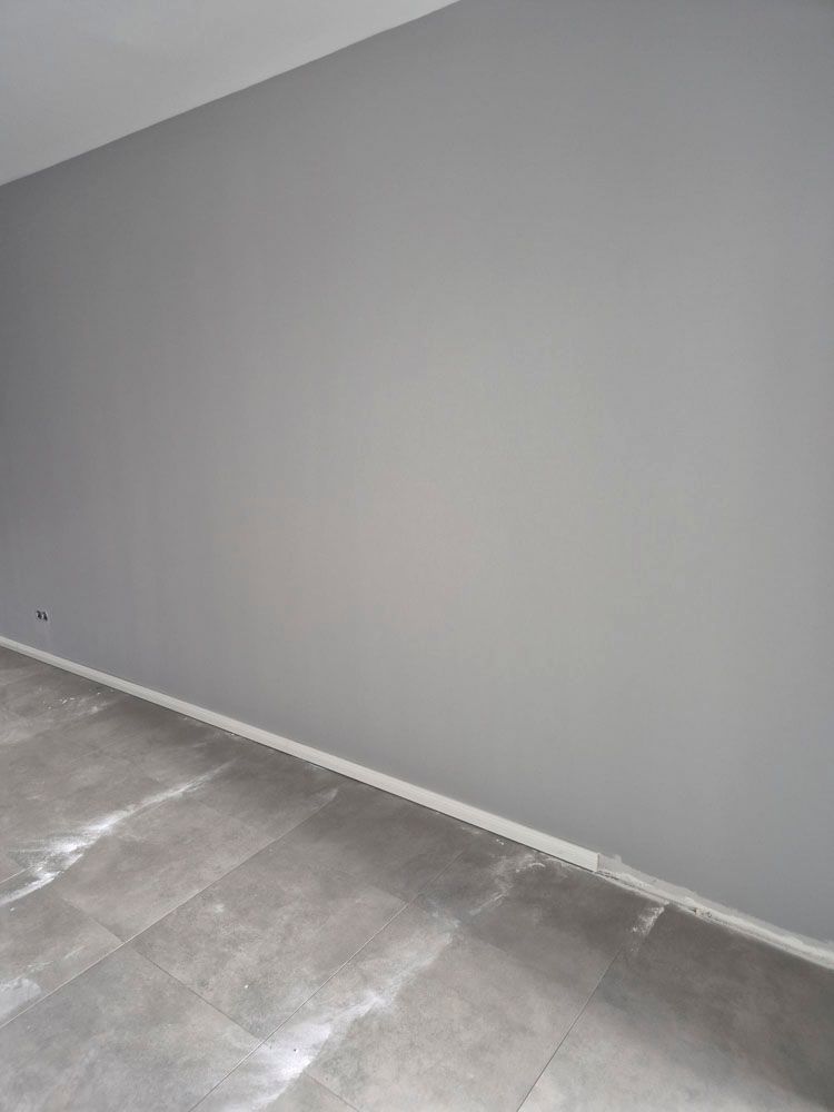 Leerer grauer Raum mit weißen Fußleisten und einem Betonboden, der renoviert wird