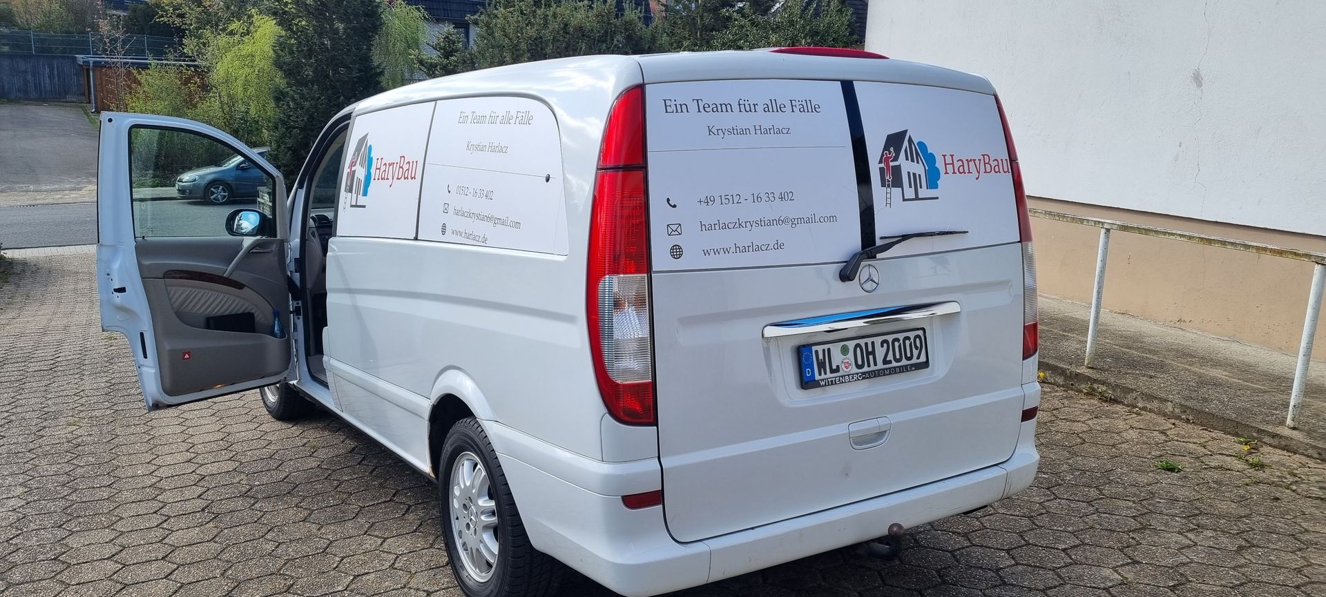 Ein weißer Lieferwagen parkt mit geöffneten Türen auf einem Kiesplatz.