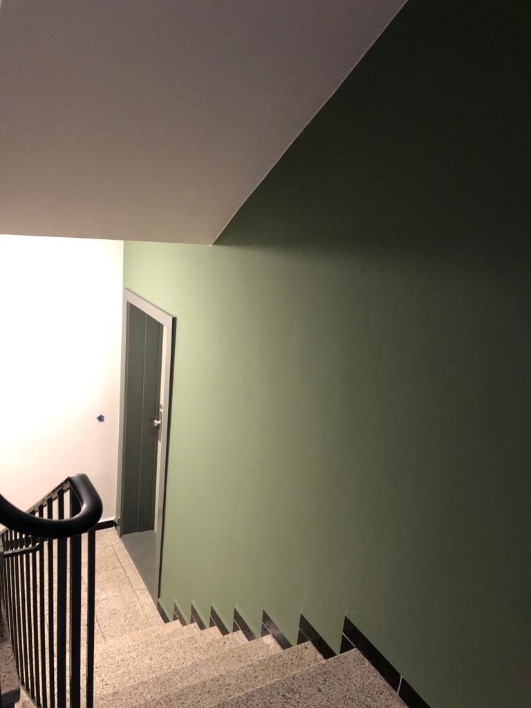 eine Treppe mit einer grünen Wand und einem schwarzen Geländer, die zu einer Tür führt.