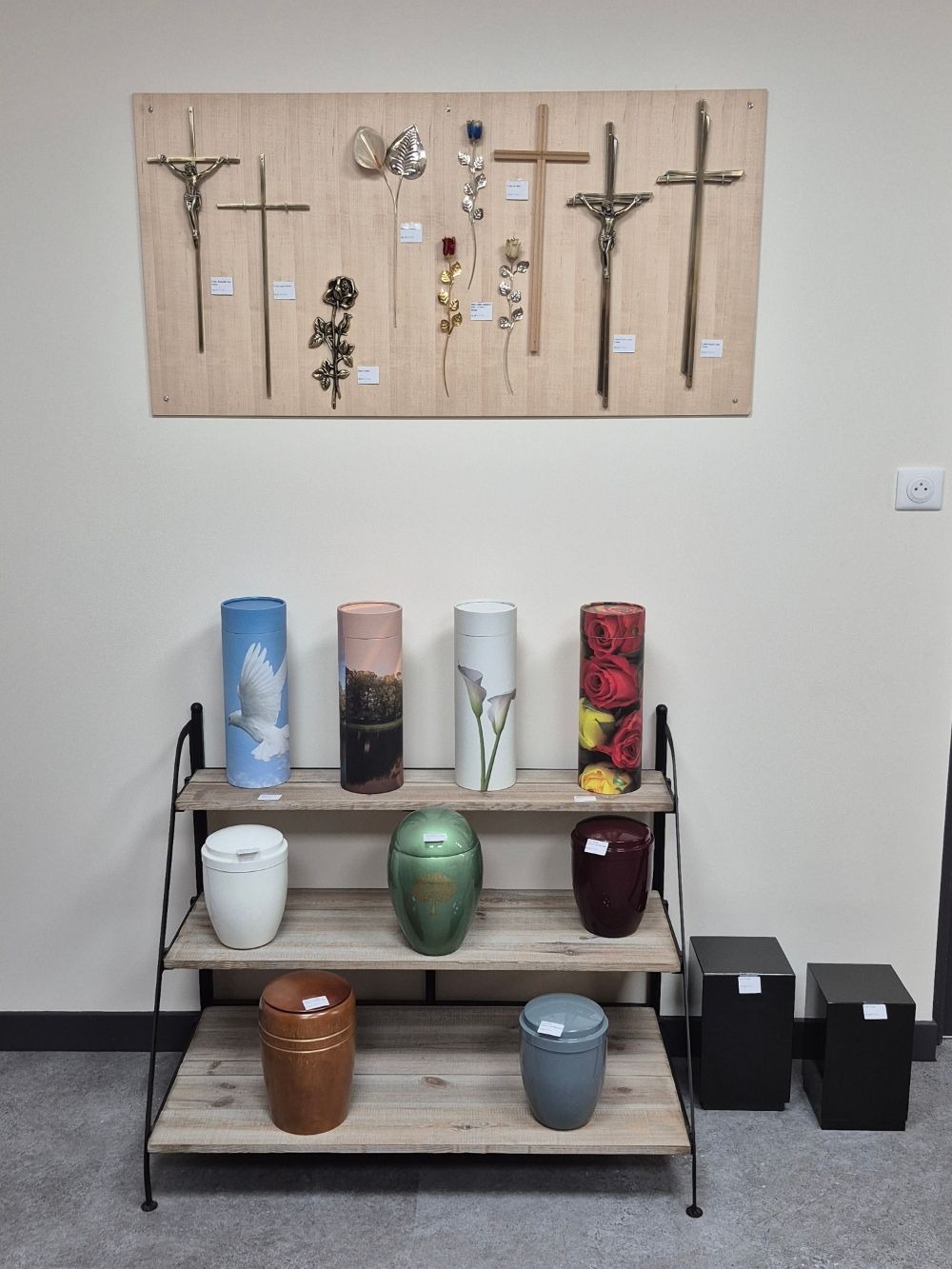 Présentation d'urnes et de croix dans un salon funéraire. Couleurs et modèles variés.