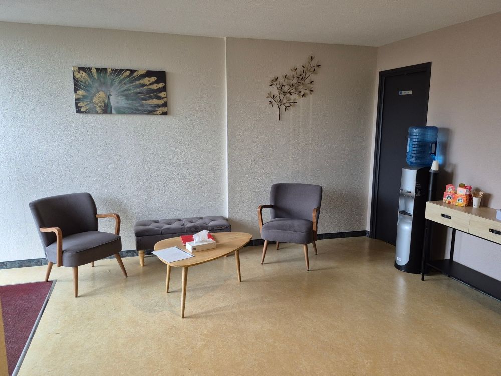 Salle d'attente : deux fauteuils, une banquette, une table basse, des œuvres d'art, une fontaine à eau. Murs beiges