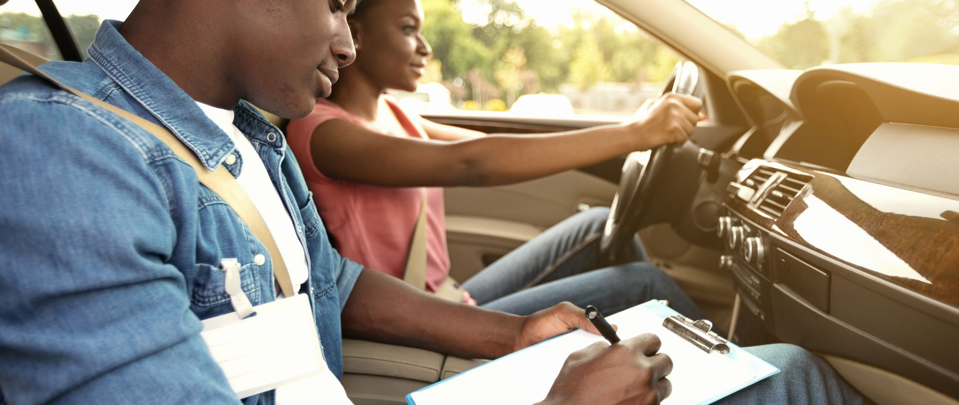 Une personne conduit une voiture avec un moniteur. Le moniteur prend des notes sur un bloc-notes. Lumière du soleil.