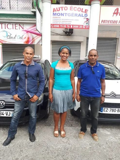 Trois personnes posent devant une auto-école et deux voitures.