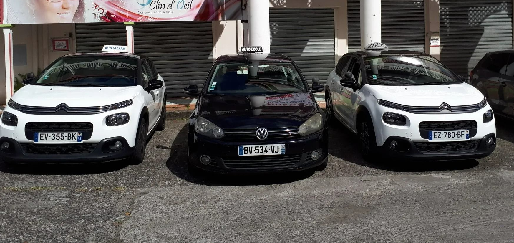 Trois voitures stationnées devant un immeuble ; deux blanches, une noire.