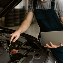 Un homme travaille sur le moteur d'une voiture tout en tenant une tablette.