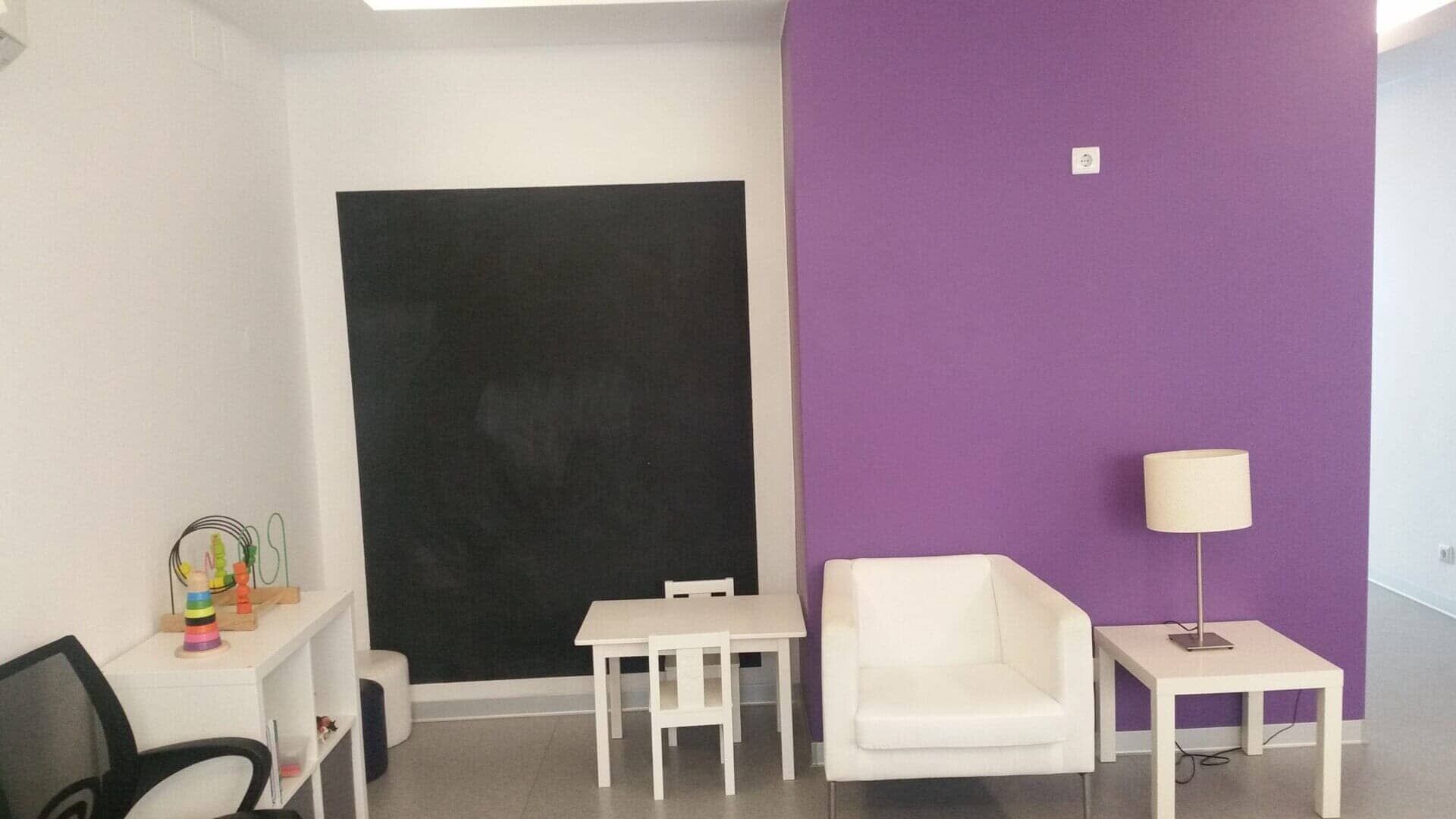 Uma sala de espera com uma parede roxa e cadeiras brancas