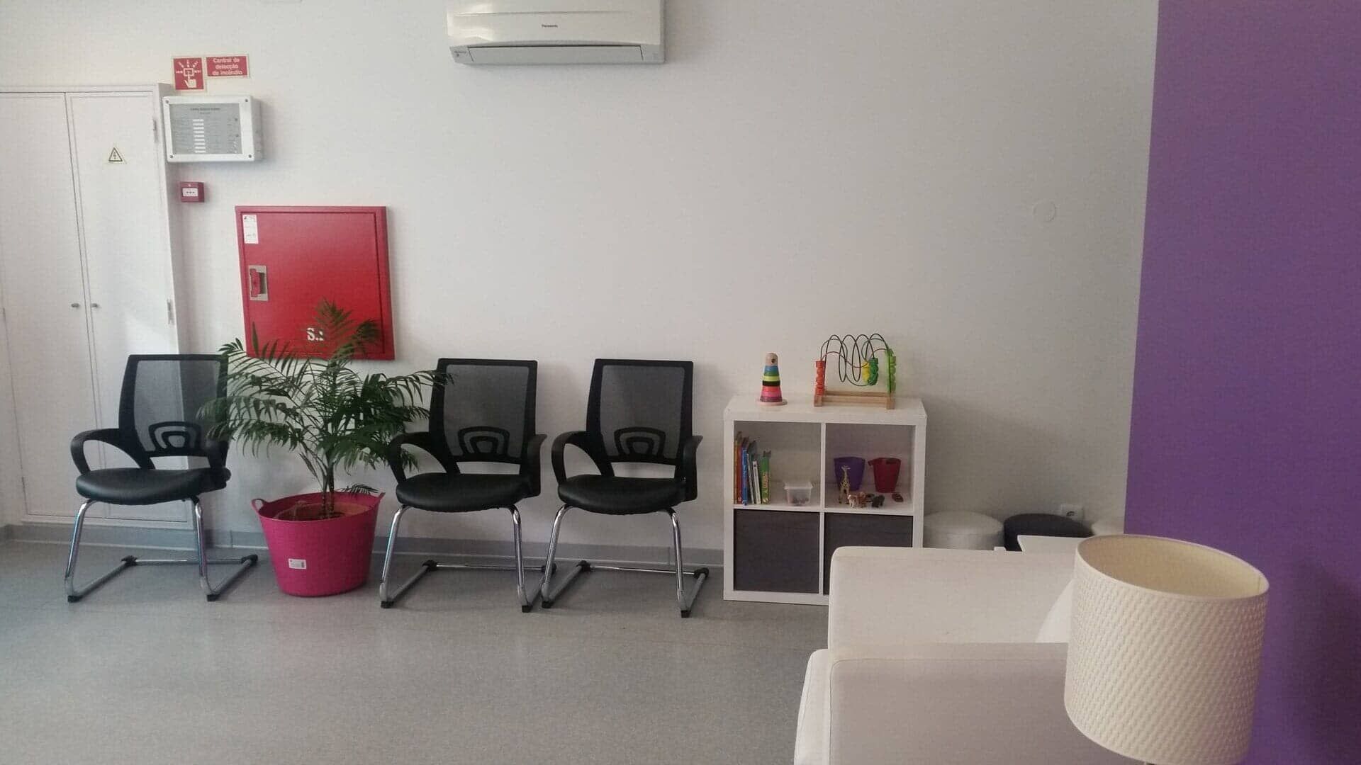 Uma sala de espera com cadeiras, uma luminária e uma parede roxa.