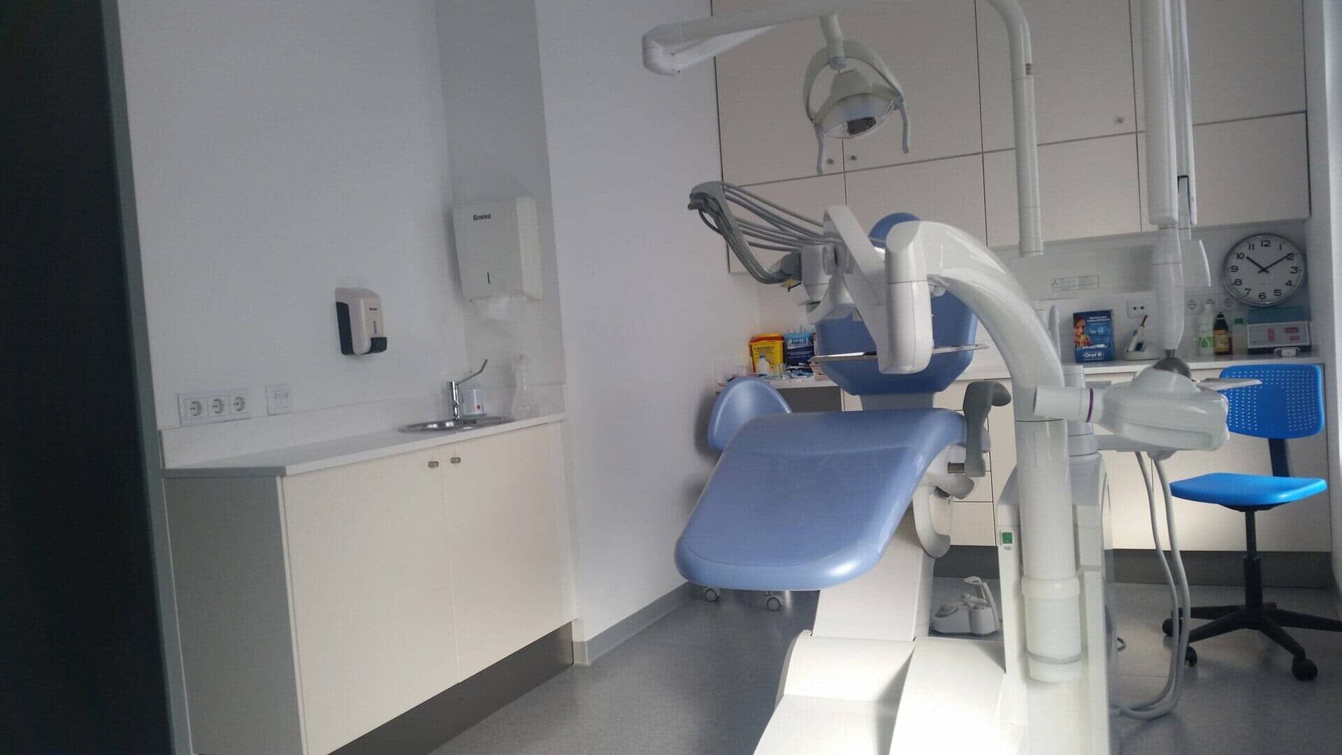 Um consultório odontológico com uma cadeira azul e uma pia