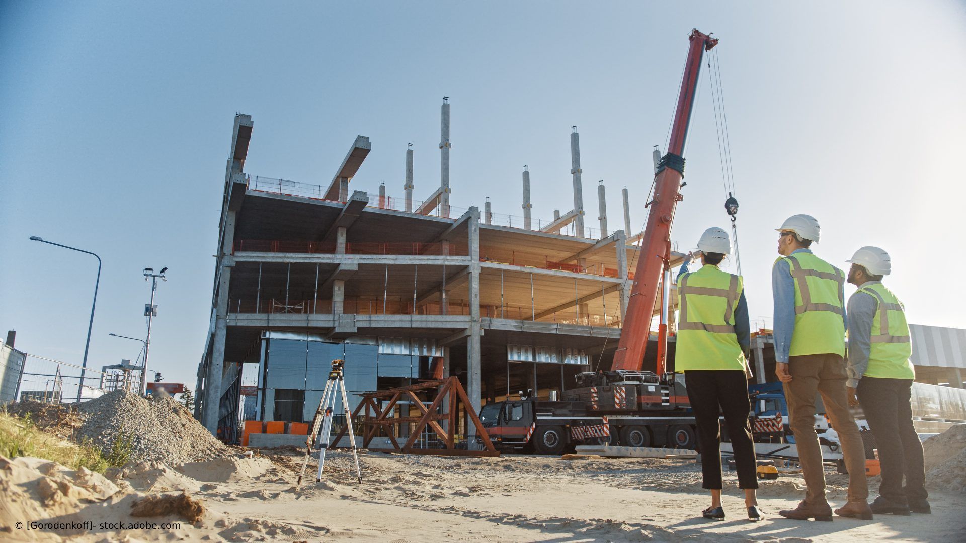 Bauarbeiter in Sicherheitswesten und Schutzhelmen an einem im Bau befindlichen Gebäude mit Kränen.