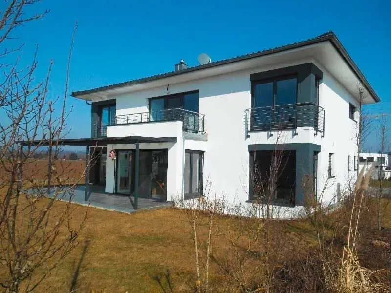 Modernes, weißes zweistöckiges Haus mit dunklen Zierelementen, Balkonen und einem kleinen Garten unter klarem, blauem Himmel