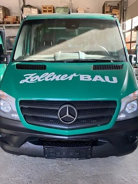 Vorderansicht eines grünen Mercedes-Transporters mit der Aufschrift „Zellner Bau“ auf der Motorhaube in einer Garage.