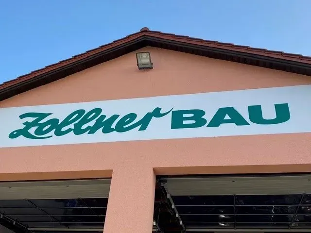 Zollner BAU-Schild an einer pfirsichfarbenen Gebäudefassade vor blauem Himmel