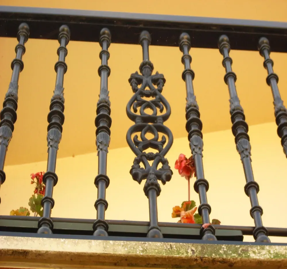 Barandilla decorativa de hierro forjado negro con flores, sobre una pared amarilla