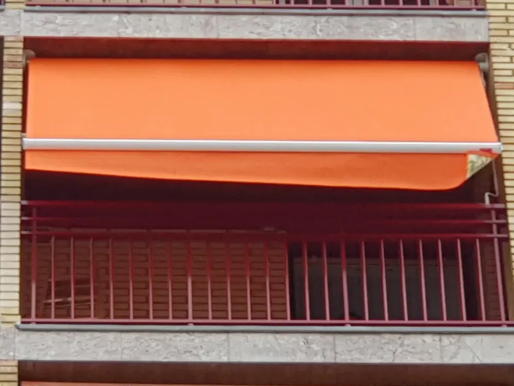 Toldo naranja retráctil sobre una barandilla metálica roja en el balcón de un edificio de ladrillo