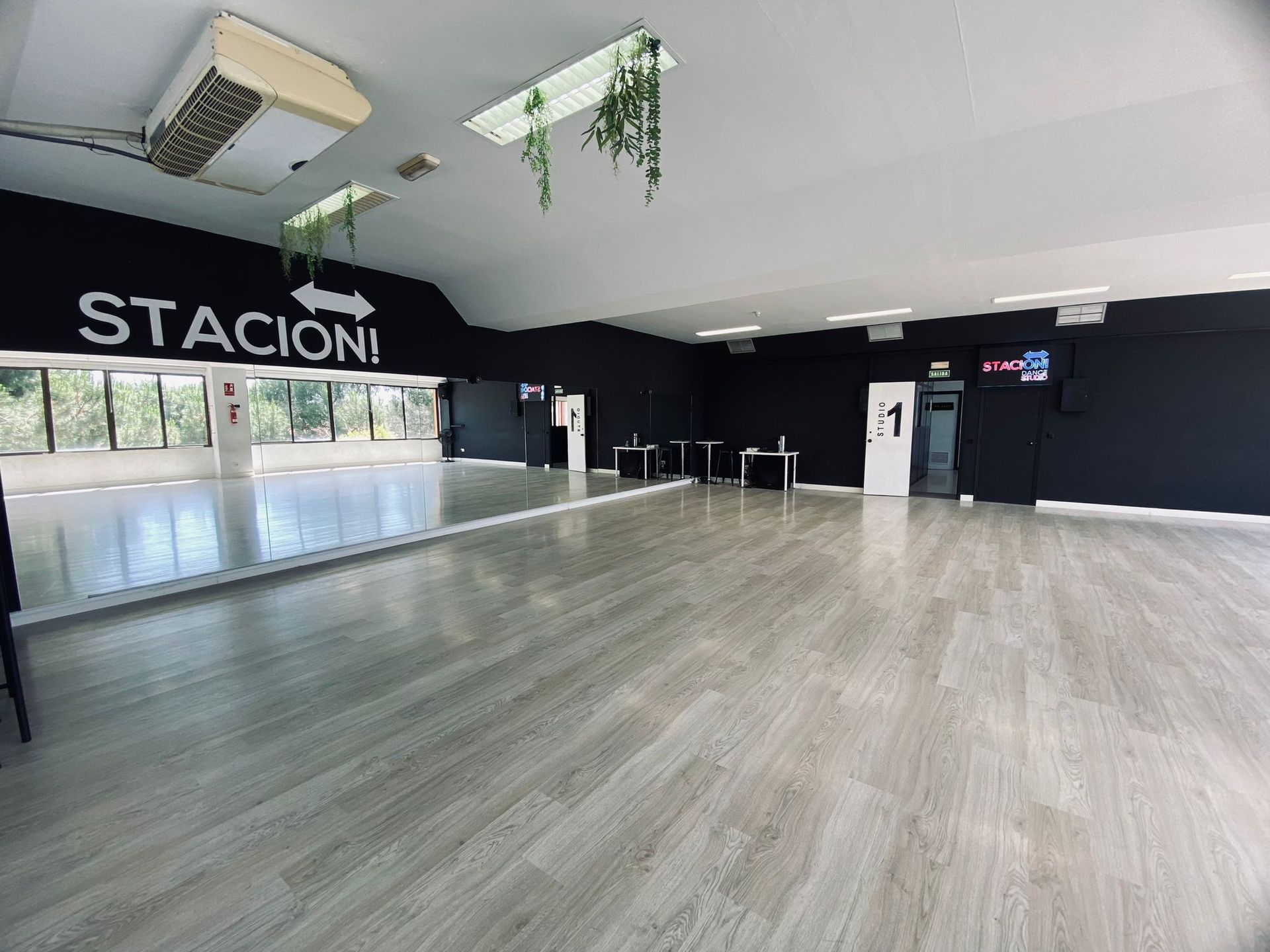 Un estudio de danza muy iluminado con suelos de madera clara, grandes espejos en las paredes y paredes negras con un letrero que dice