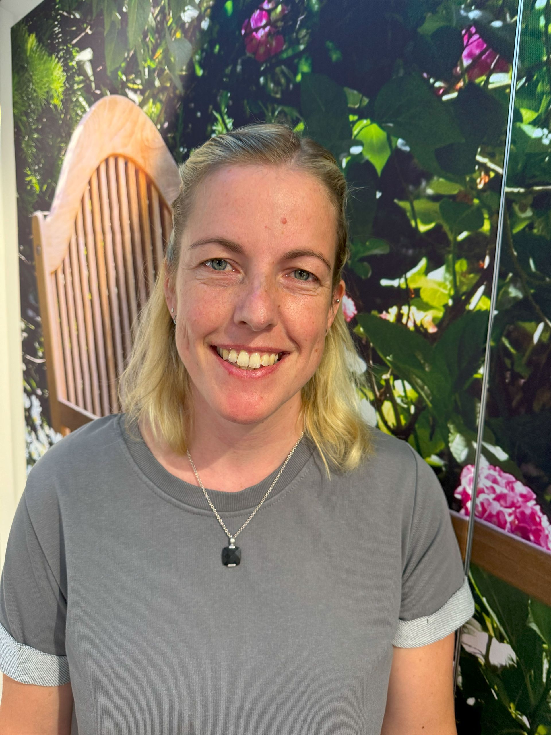 Eine Frau lächelt vor einem Blumenbild an einer Wand.