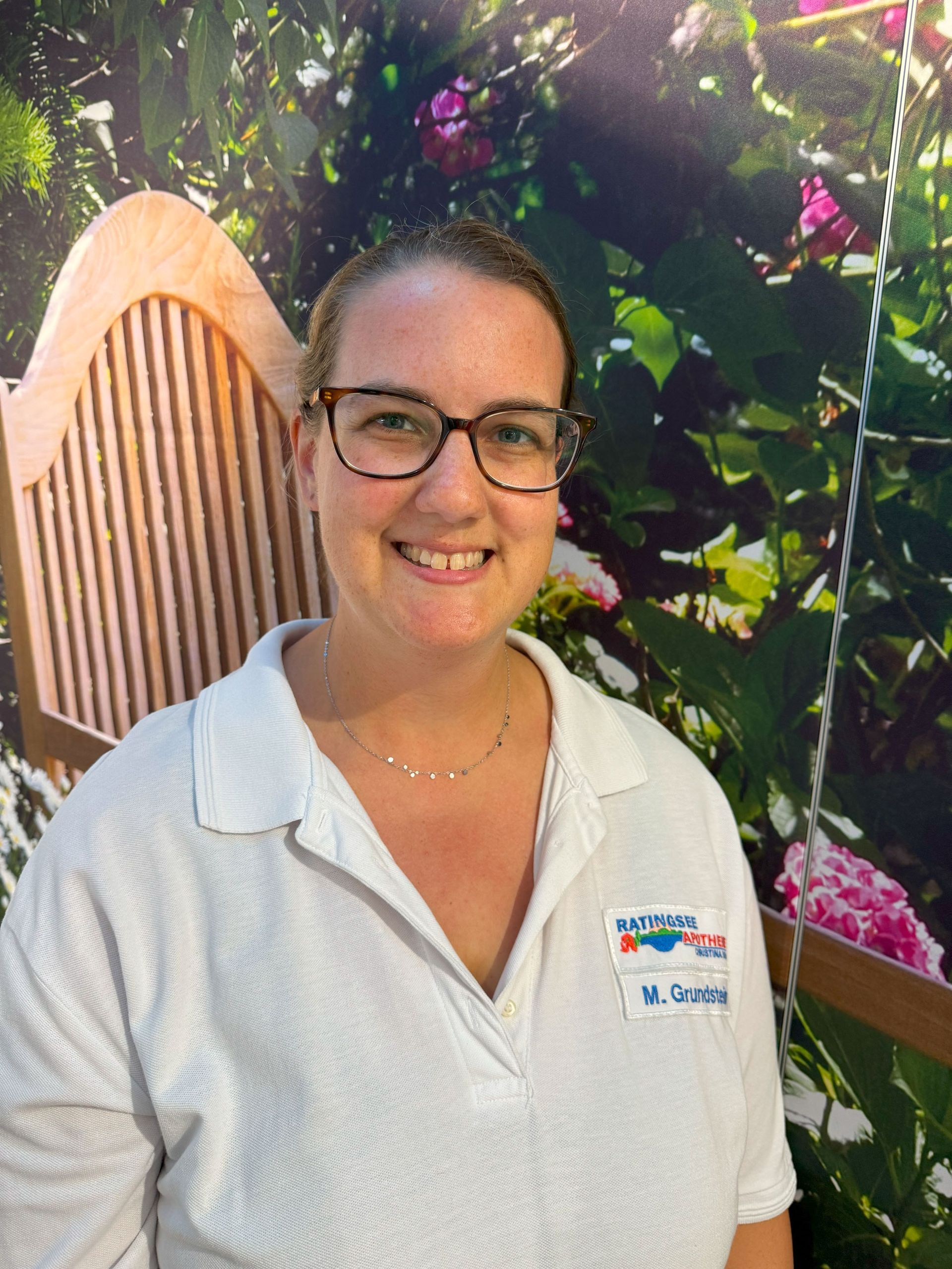 Eine Frau mit Brille und weißem Hemd lächelt vor einem Blumenbild.