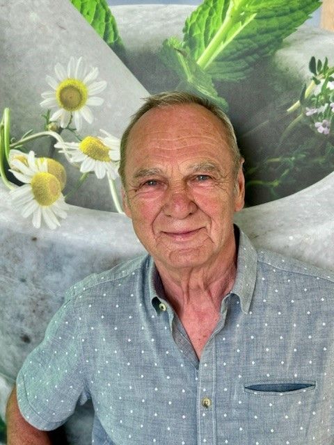 Ein Mann in einem blauen Hemd steht vor einem Bild mit Gänseblümchen.