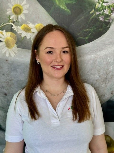 Eine Frau in einem weißen Hemd lächelt vor einem Bild mit Gänseblümchen.