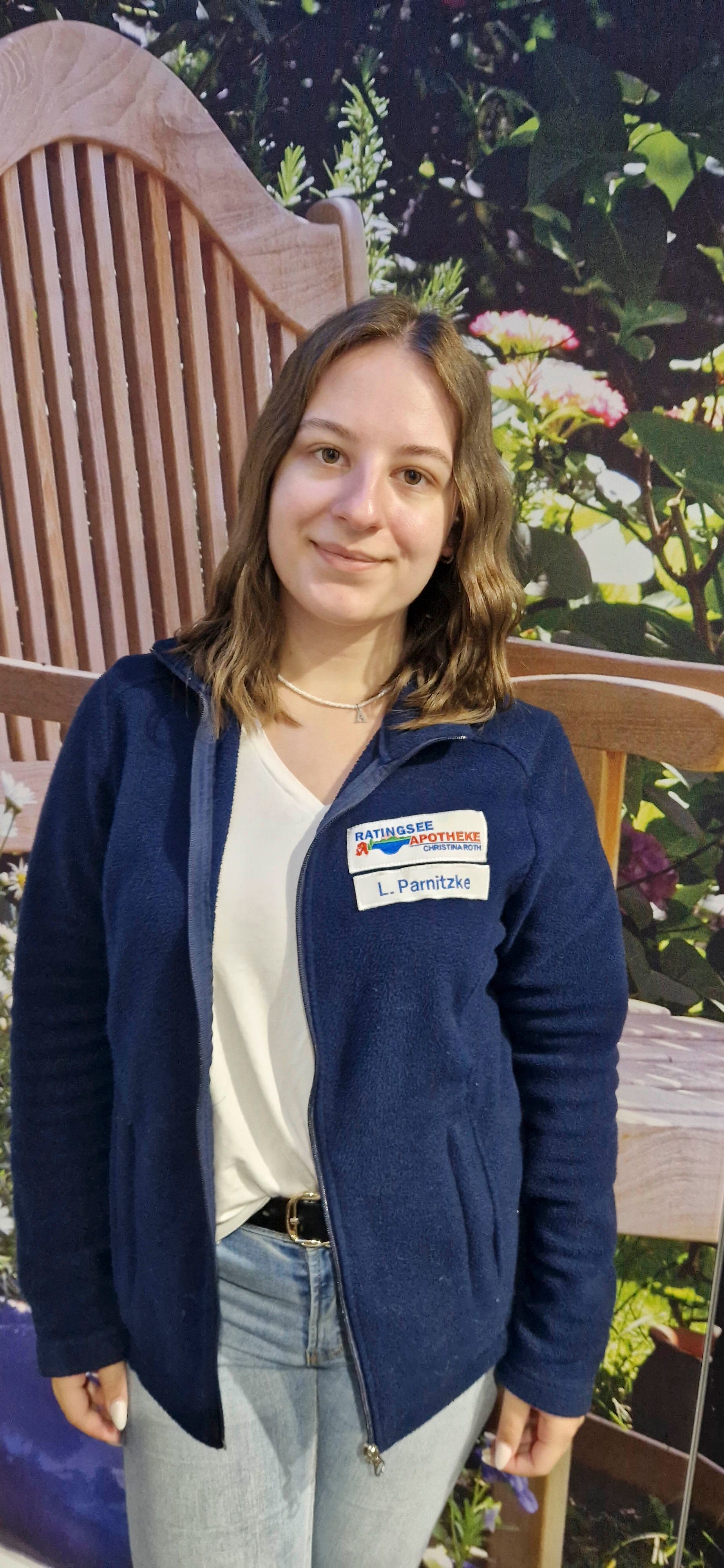 Eine Frau in einer blauen Jacke steht vor einer Holzbank.