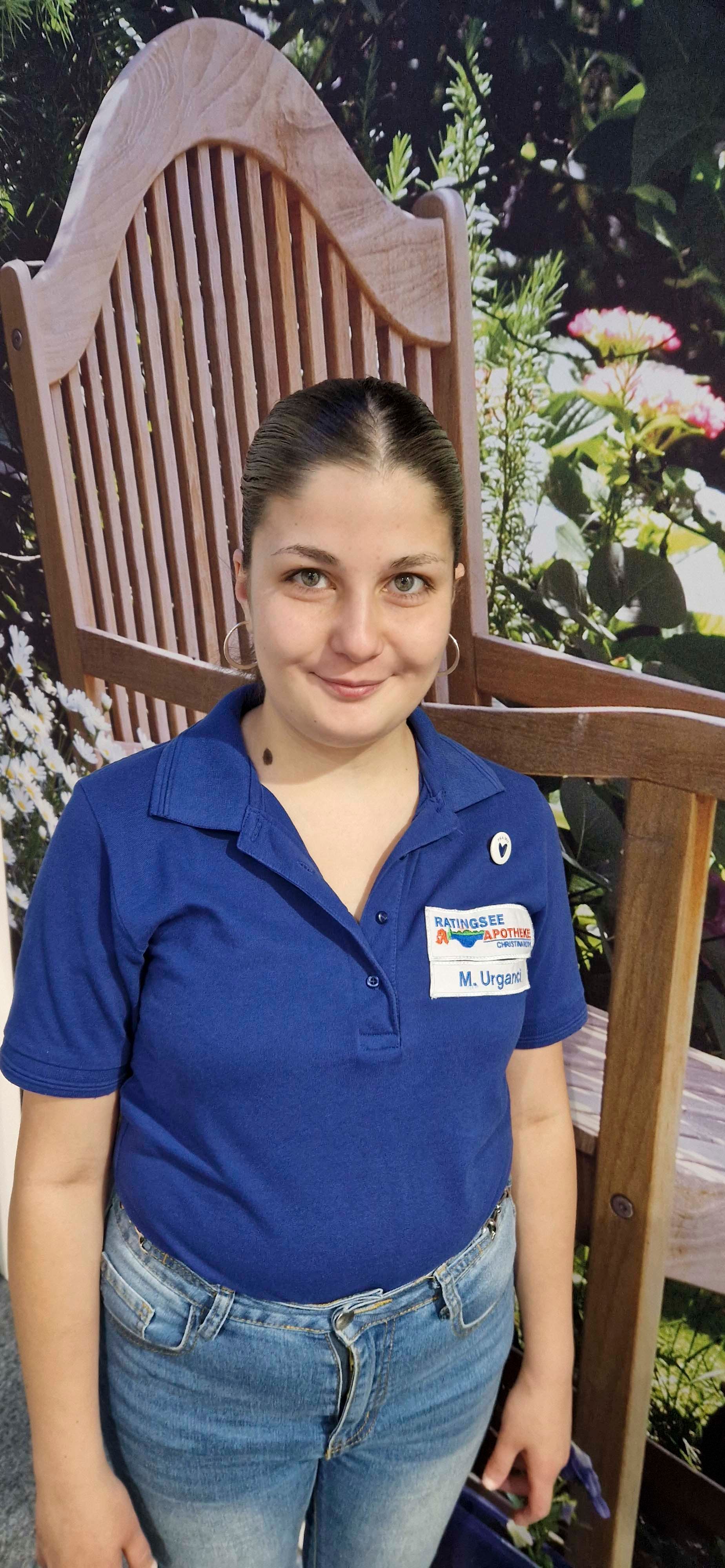 Eine Frau in einem blauen Hemd steht vor einem Holzstuhl.