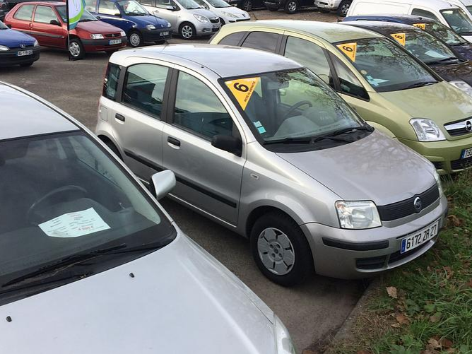 Voiture compacte argentée dans un parking bondé, entourée d'autres véhicules.