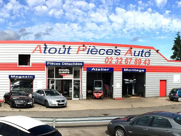 Vue extérieure du garage Atout Pièces Auto avec le bâtiment principal, l’atelier, le magasin et plusieurs véhicules stationnés devant.