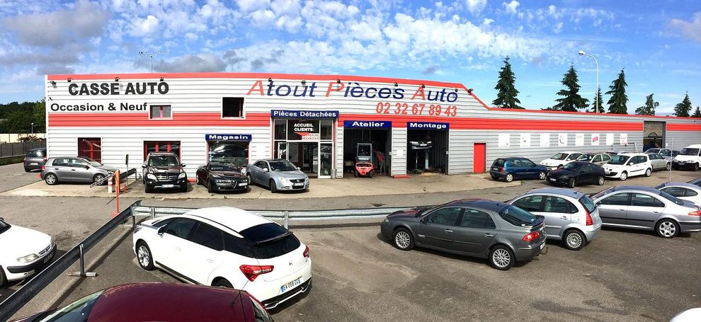 Atelier de pneus et de réparation automobile avec une enseigne rouge et blanche et plusieurs voitures garées devant.