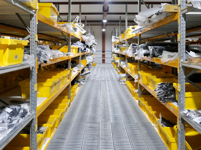 Allée de stockage avec étagères métalliques et bacs jaunes remplis de pièces emballées.