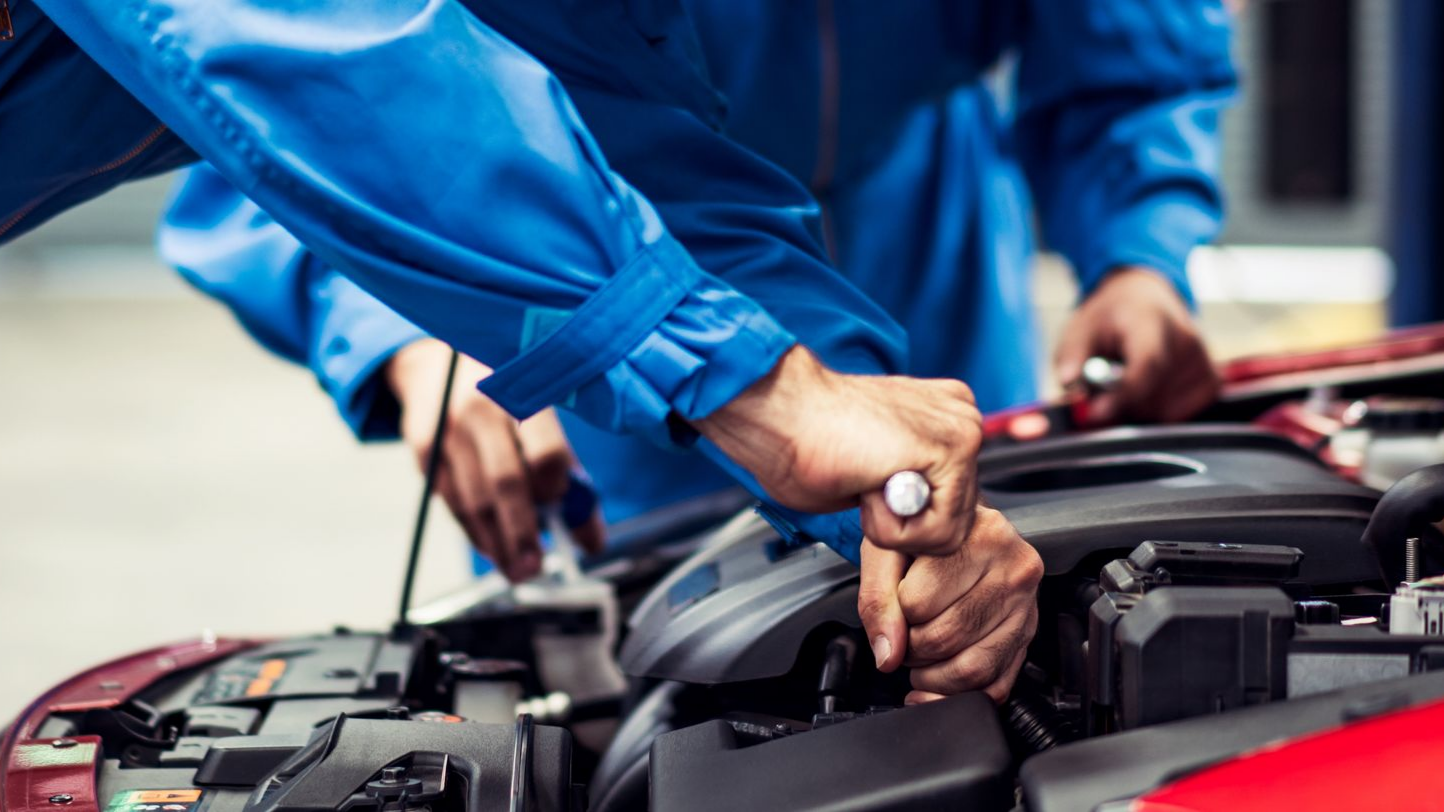 Deux garagistes en blouse bleue au-dessus d'une voiture rouge