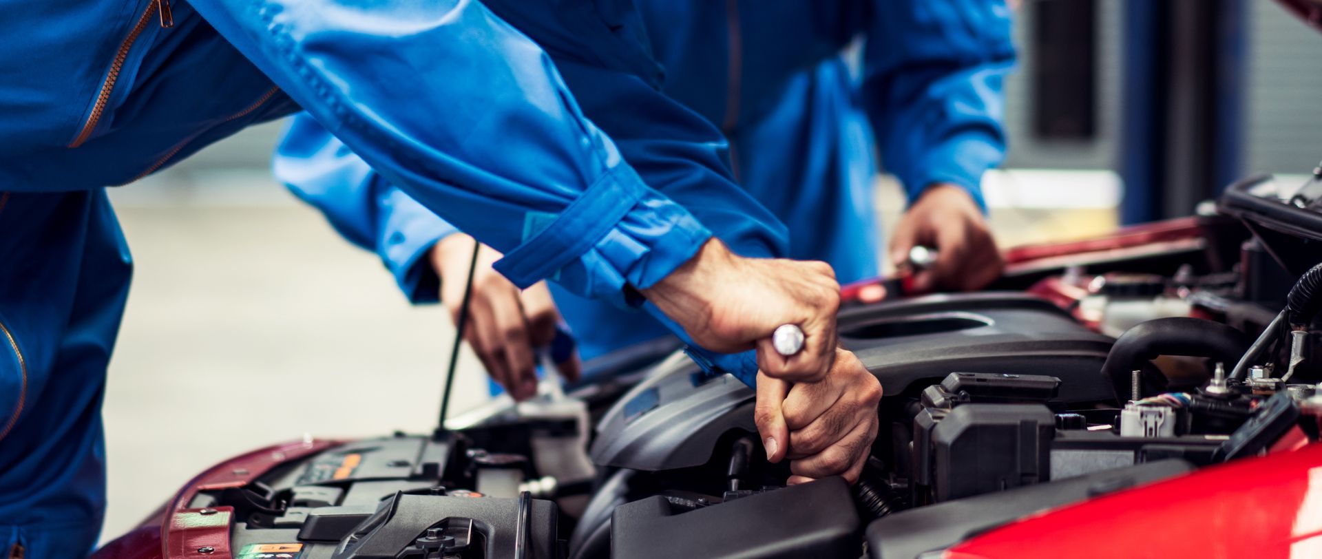 Un mécanicien en uniforme bleu travaille sous le capot d'une voiture avec des outils dans un atelier