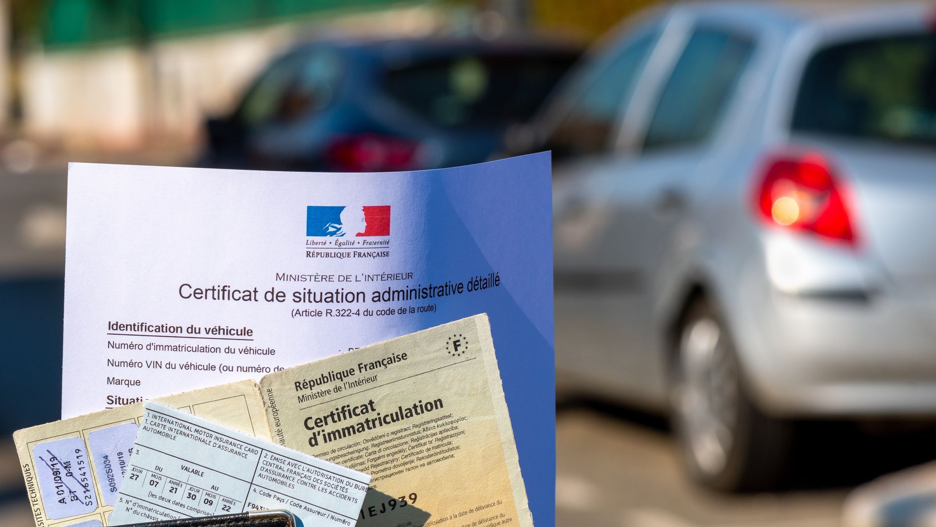 Des papiers d'identité français devant une voiture argentée floue avec des feux arrière rouges.
