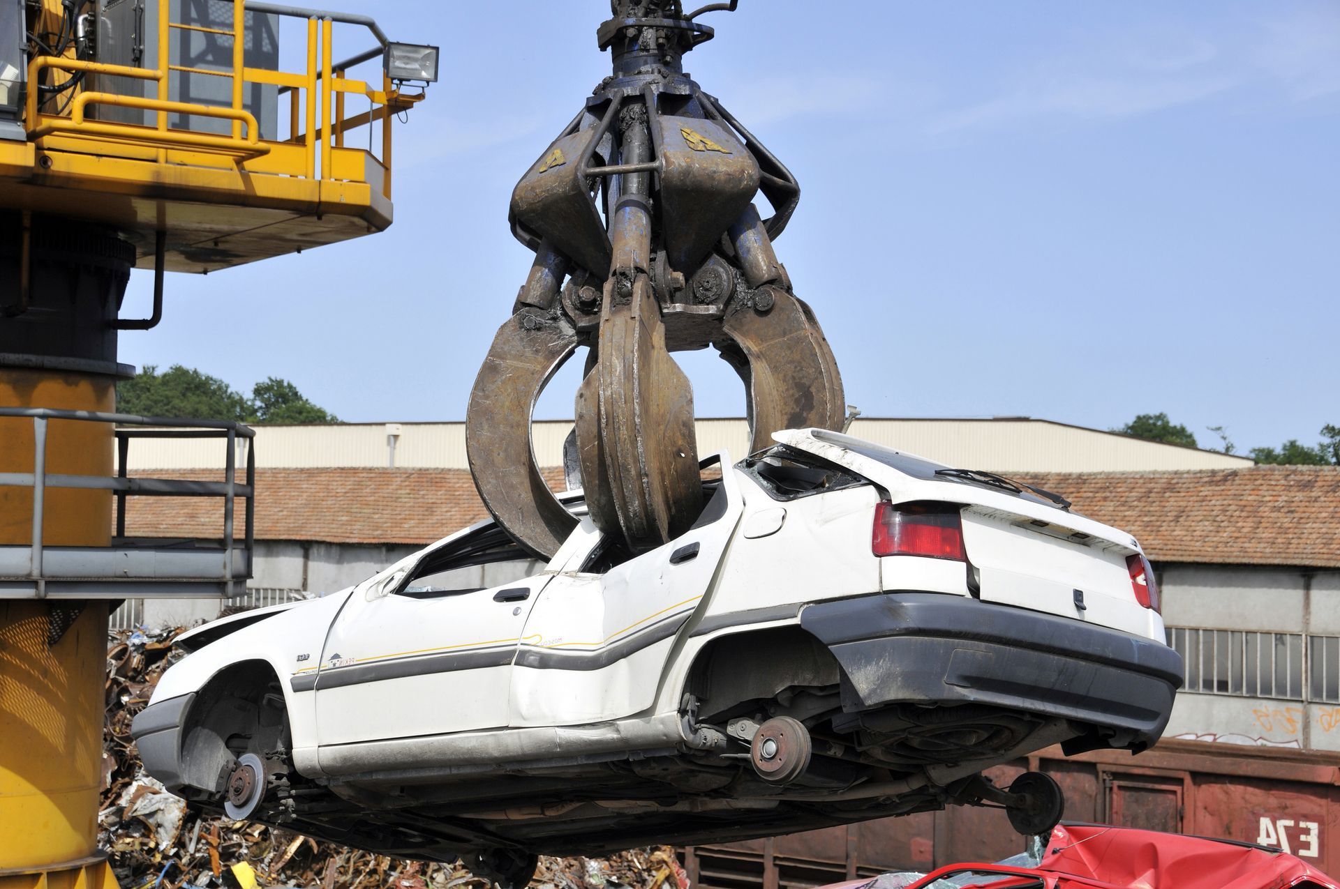 Une grue soulève une voiture blanche accidentée dans une zone industrielle.
