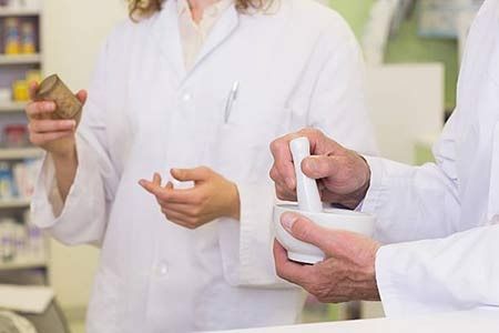 Una farmacéutica sostiene un frasco de pastillas y un mortero.