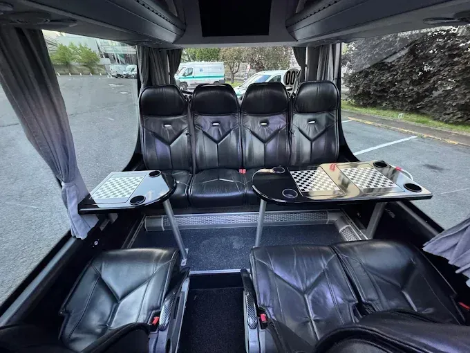 Intérieur d'un van de luxe avec sièges en cuir noir et tables rabattables, vu de l'arrière vers l'avant.