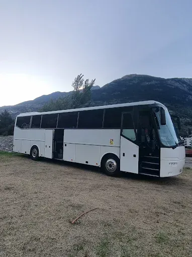 Autocar blanc stationné sur un terrain gravillonné, avec des montagnes en arrière-plan au crépuscule