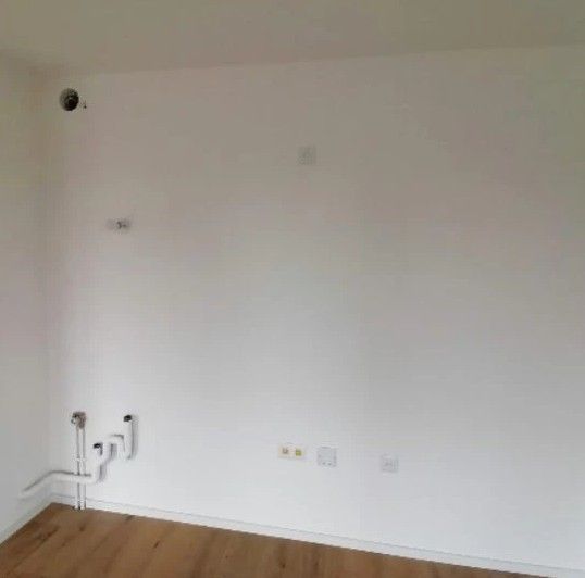 Pièce blanche vide avec parquet et prises murales près des plinthes