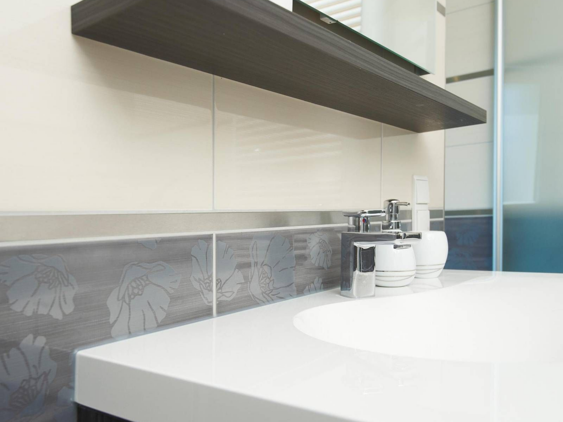 Meuble-lavabo moderne avec plan de toilette blanc, crédence grise à motifs floraux, étagère et produits de toilette